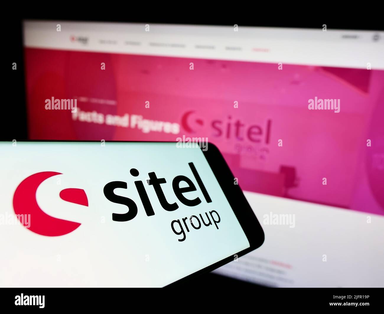 Téléphone portable avec logo de la société américaine de centre de contact Sitel Group à l'écran en face du site Web d'affaires. Effectuez la mise au point au centre-droit de l'écran du téléphone. Banque D'Images