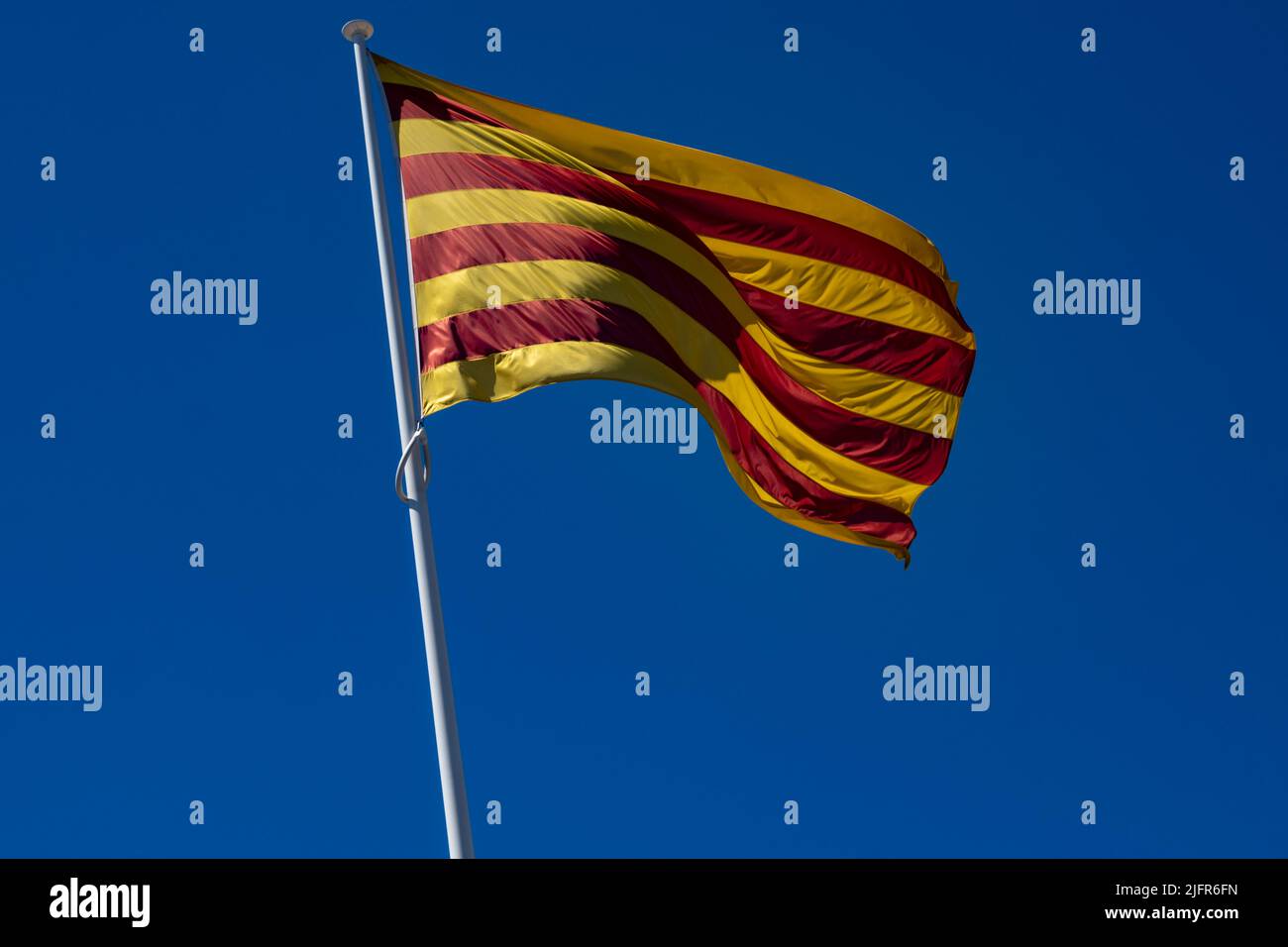 Le drapeau de la Catalogne (Communauté autonome d'Espagne) agitant dans un ciel bleu profond. Mât incliné vers la gauche. Banque D'Images
