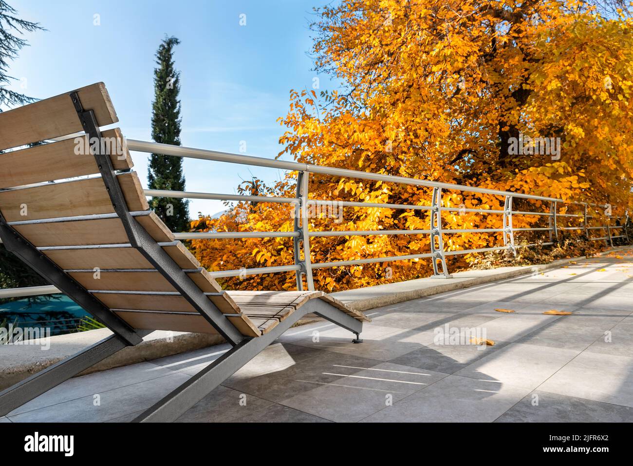 Vue rapprochée de la chaise longue vide moderne en bois sur le patio balcon terrasse contre l'arbre d'automne jaune vif et le ciel bleu. Vacances d'automne Banque D'Images