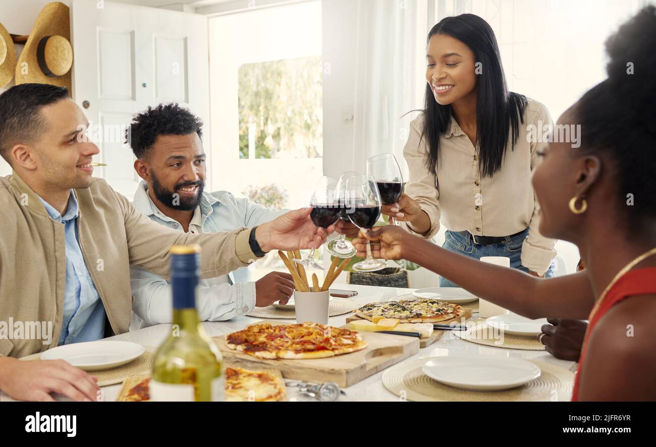 Partager un toast au nom de l'amitié. Photo d'un groupe de personnes partageant un toast autour de la table à manger dans une maison. Banque D'Images