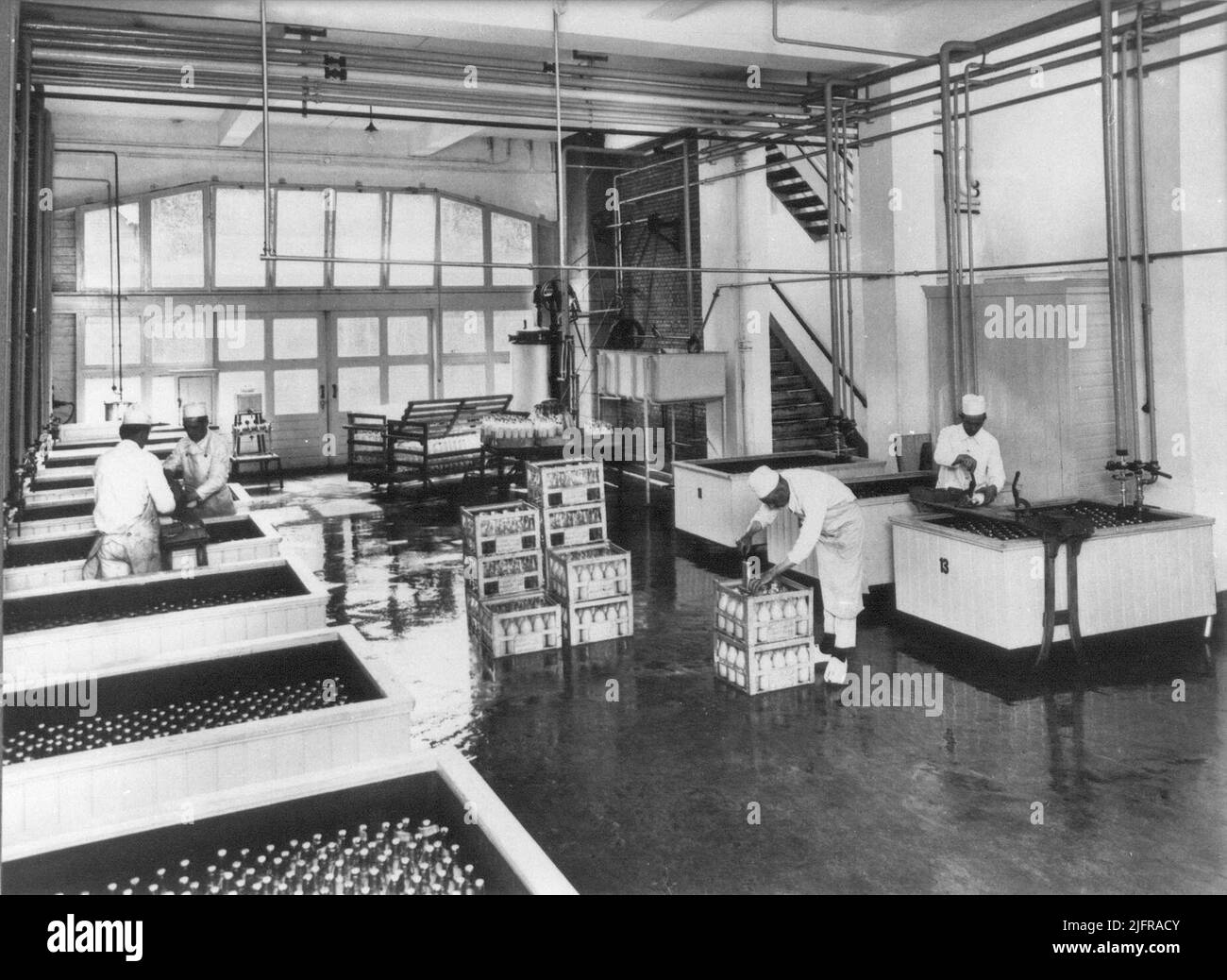 Salle de pasteurisation des bouteilles. Paper, machine de remplissage, plateaux de pasteurisation et comptoirs avec une salle de lait derrière elle. Banque D'Images