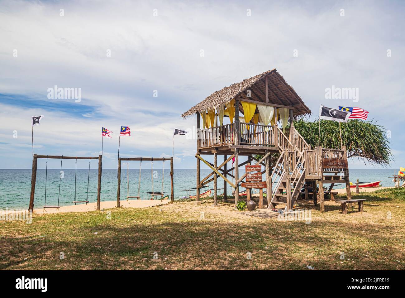Cabane de plage sur pilotis, balançoires et drapeaux sur la plage de Pantai Jambu Bongkok Beach à Terengganu, Malaisie. Banque D'Images