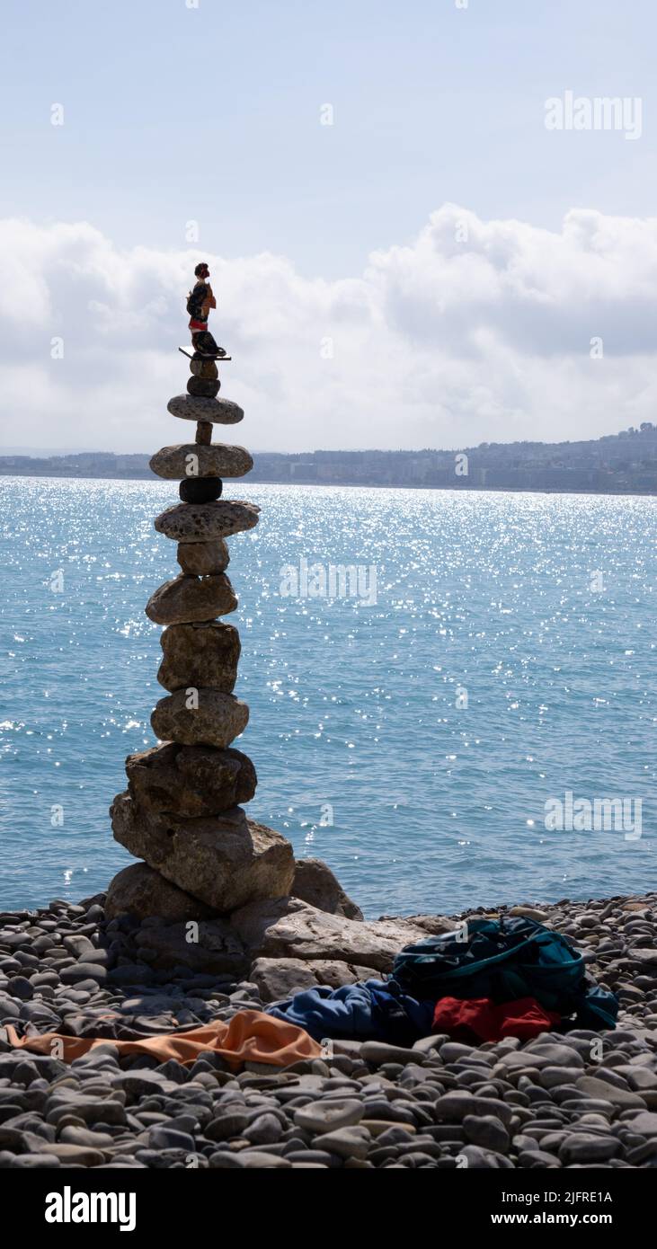 Un homme qui a laissé ses vêtements sur les pierres de la plage et a patiemment commencé à construire cette tour de rochers placés dans un équilibre parfait. Banque D'Images