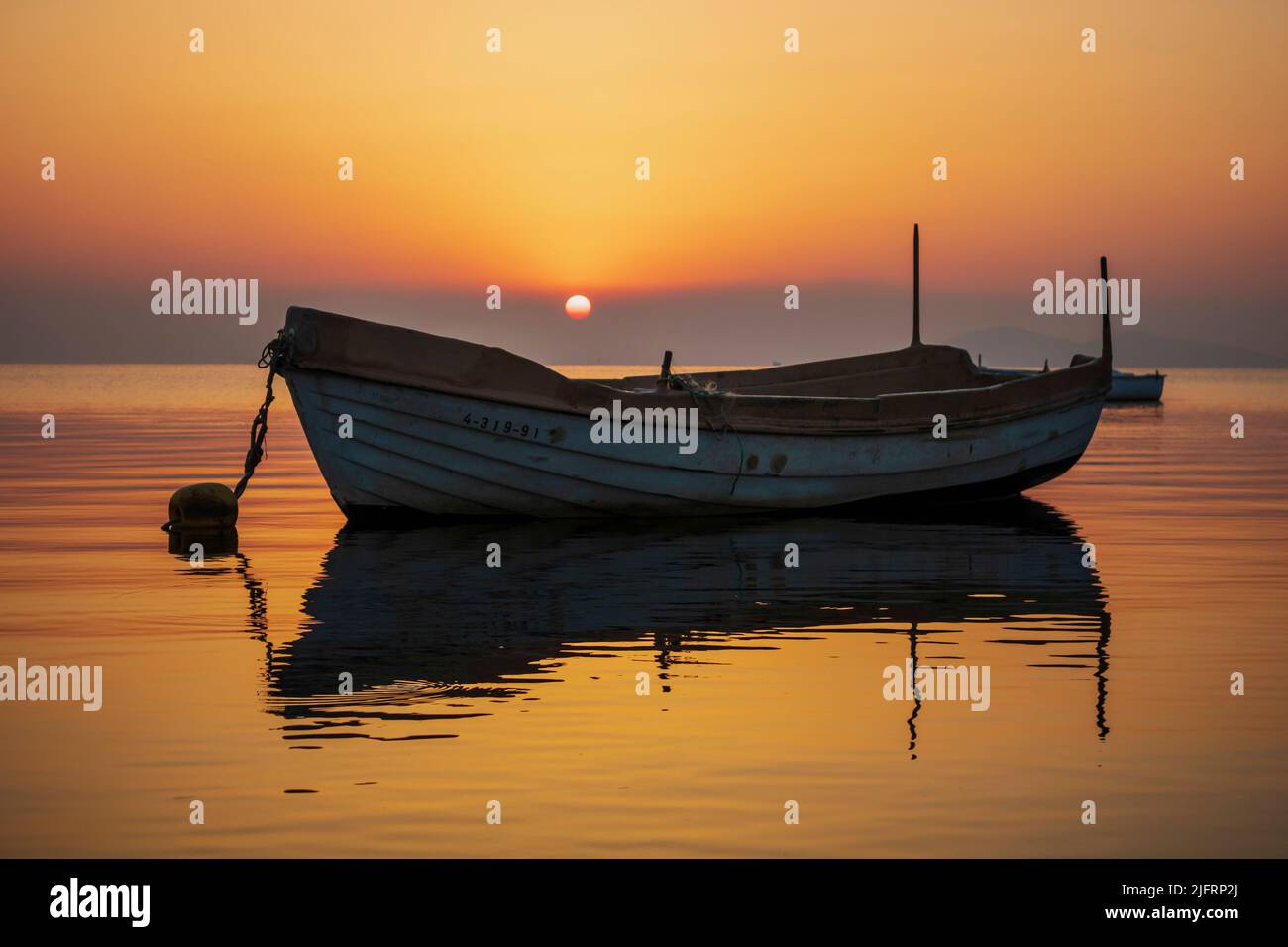 Photographie horizontale d'un lever de soleil dans la Mar Menor de Murcia, Espagne, avec un bateau de pêche en premier plan et un ciel orange et jaune qui est refait Banque D'Images