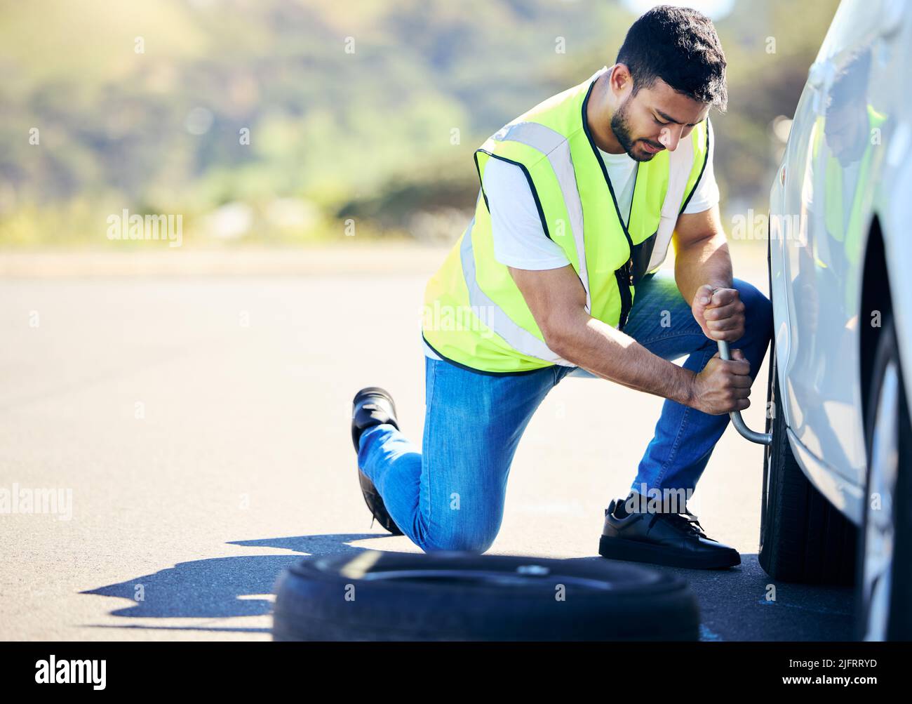 Il est impossible de découvrir de beaux chemins sans avoir à se faire des los. Photo d'un jeune homme changeant un pneu crevé sur sa voiture dans une zone rurale. Banque D'Images