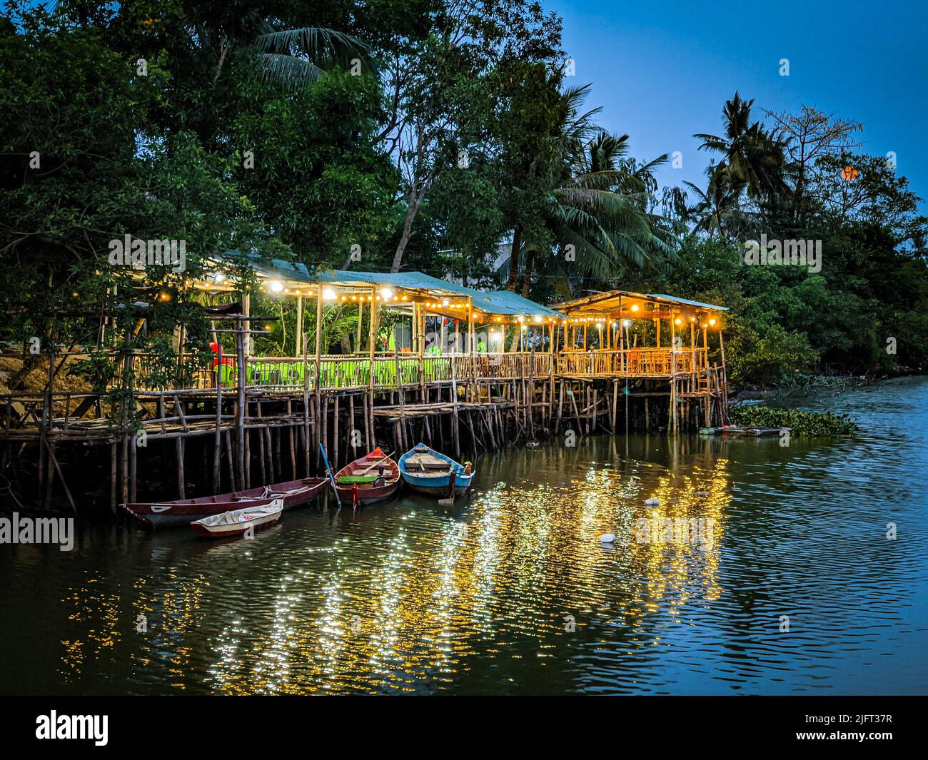 Une belle photo de bateaux et de lumières dans un cottage en bambou flottant sur une rivière au crépuscule Banque D'Images