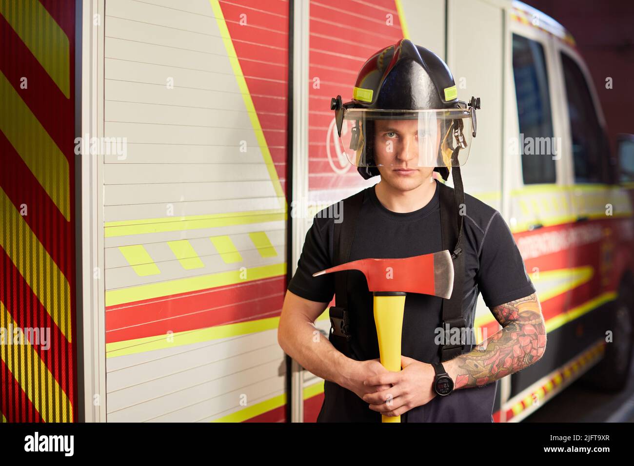 Photo d'un pompier portant un casque avec une hache contre un moteur d'incendie. Banque D'Images