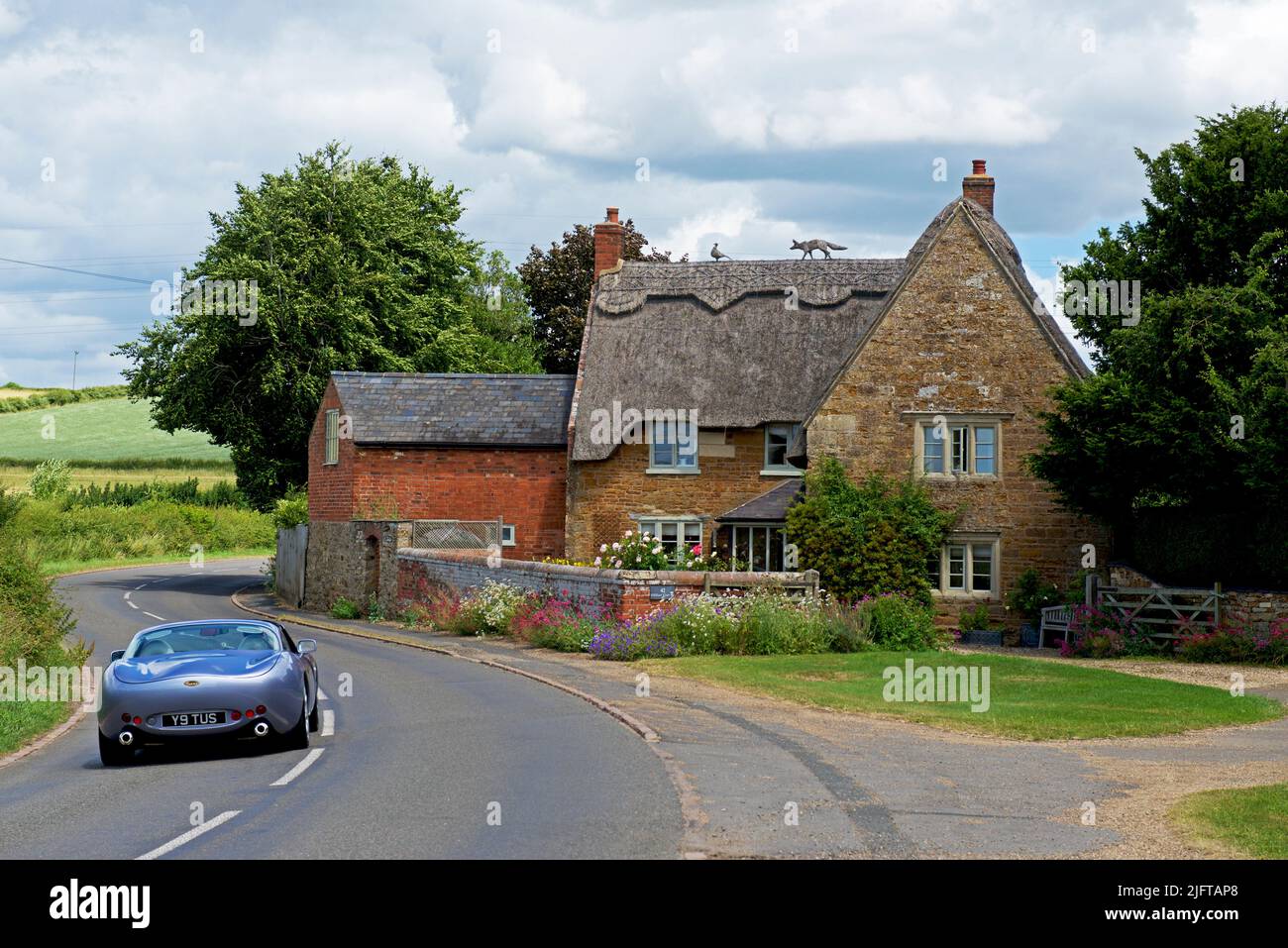 TVR voiture de sport toscane approchant d'un chalet de chaume dans le village de Sutton Bassett, Northamptonshire, Angleterre Royaume-Uni Banque D'Images