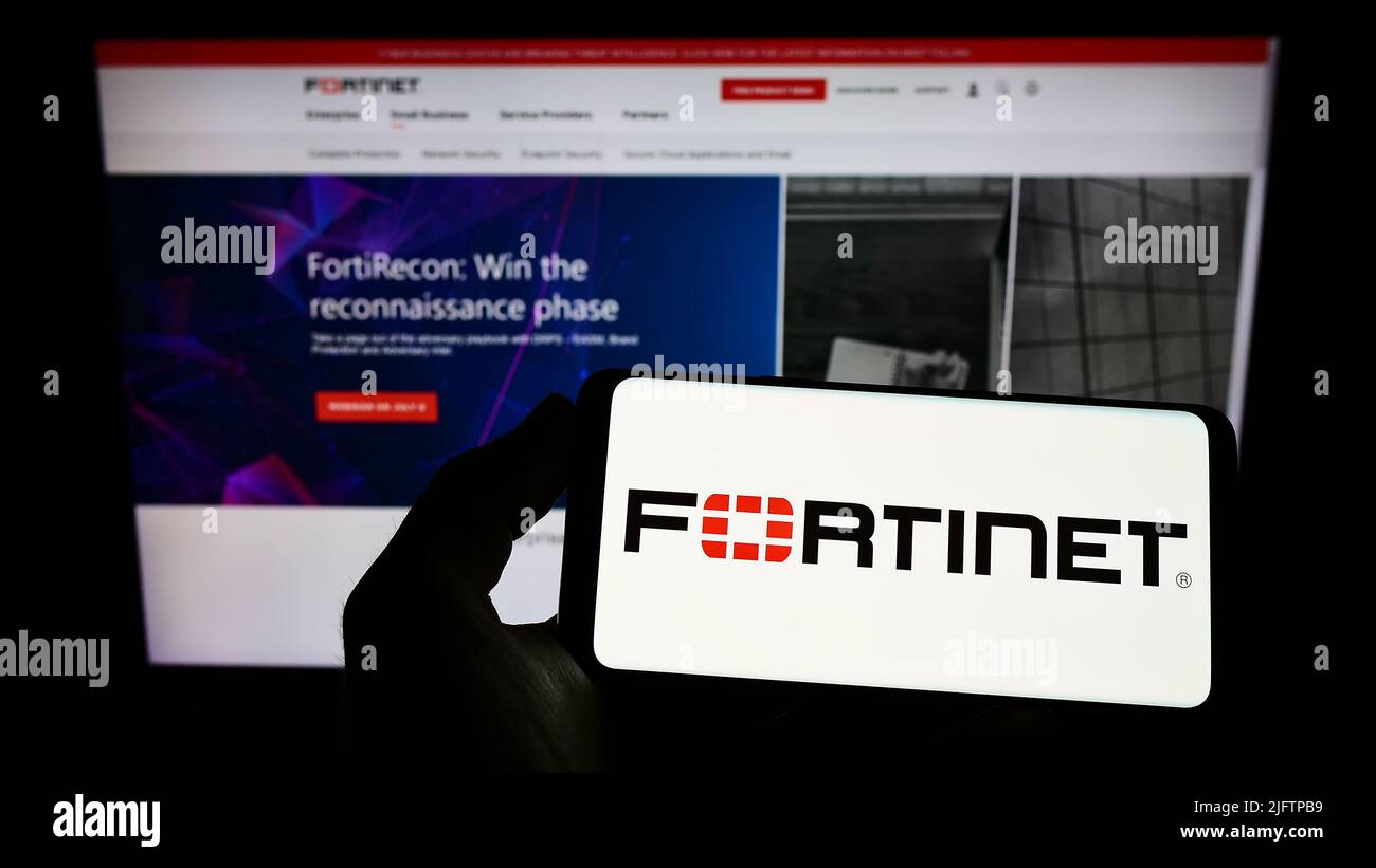 Personne portant un smartphone portant le logo de la société américaine de cybersécurité Fortinet Inc. À l'écran devant le site Web. Mise au point sur l'affichage du téléphone. Banque D'Images