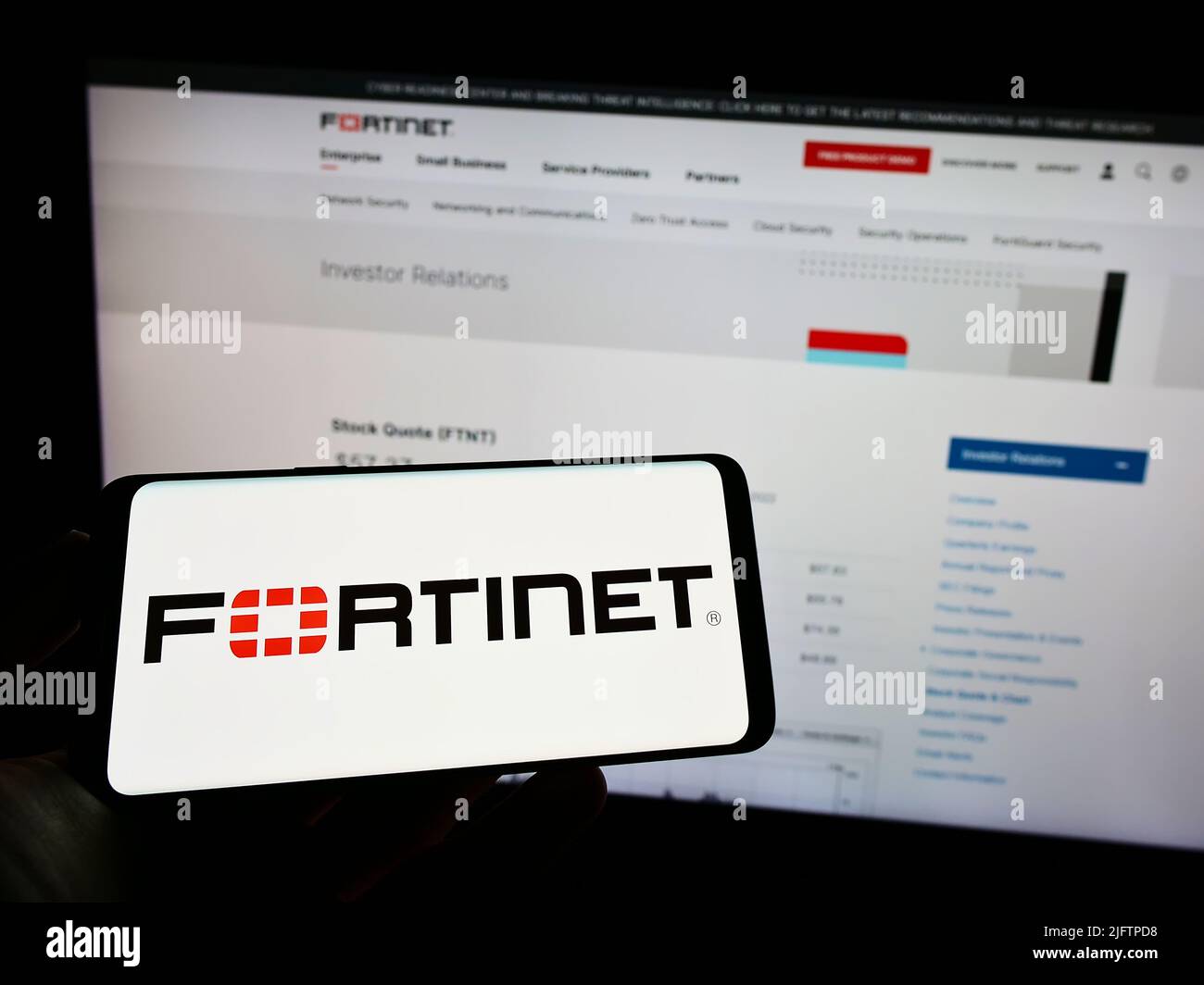 Personne tenant un téléphone portable avec le logo de la société américaine de cybersécurité Fortinet Inc. À l'écran en face de la page Web des affaires. Mise au point sur l'affichage du téléphone. Banque D'Images
