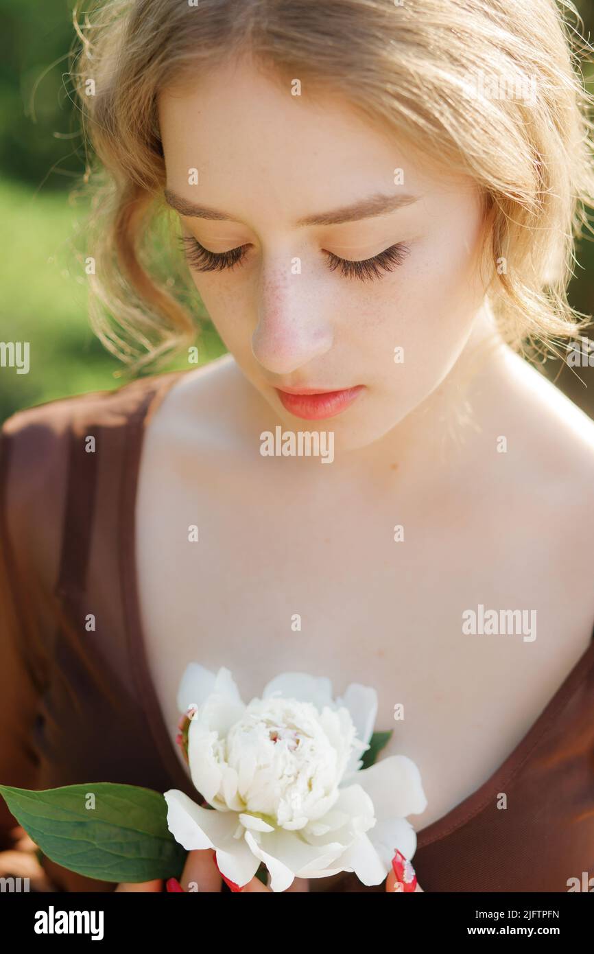 Portrait en gros plan d'une jolie blonde avec une fleur blanche dans sa main. Ton vintage. Arrière-plan flou Banque D'Images