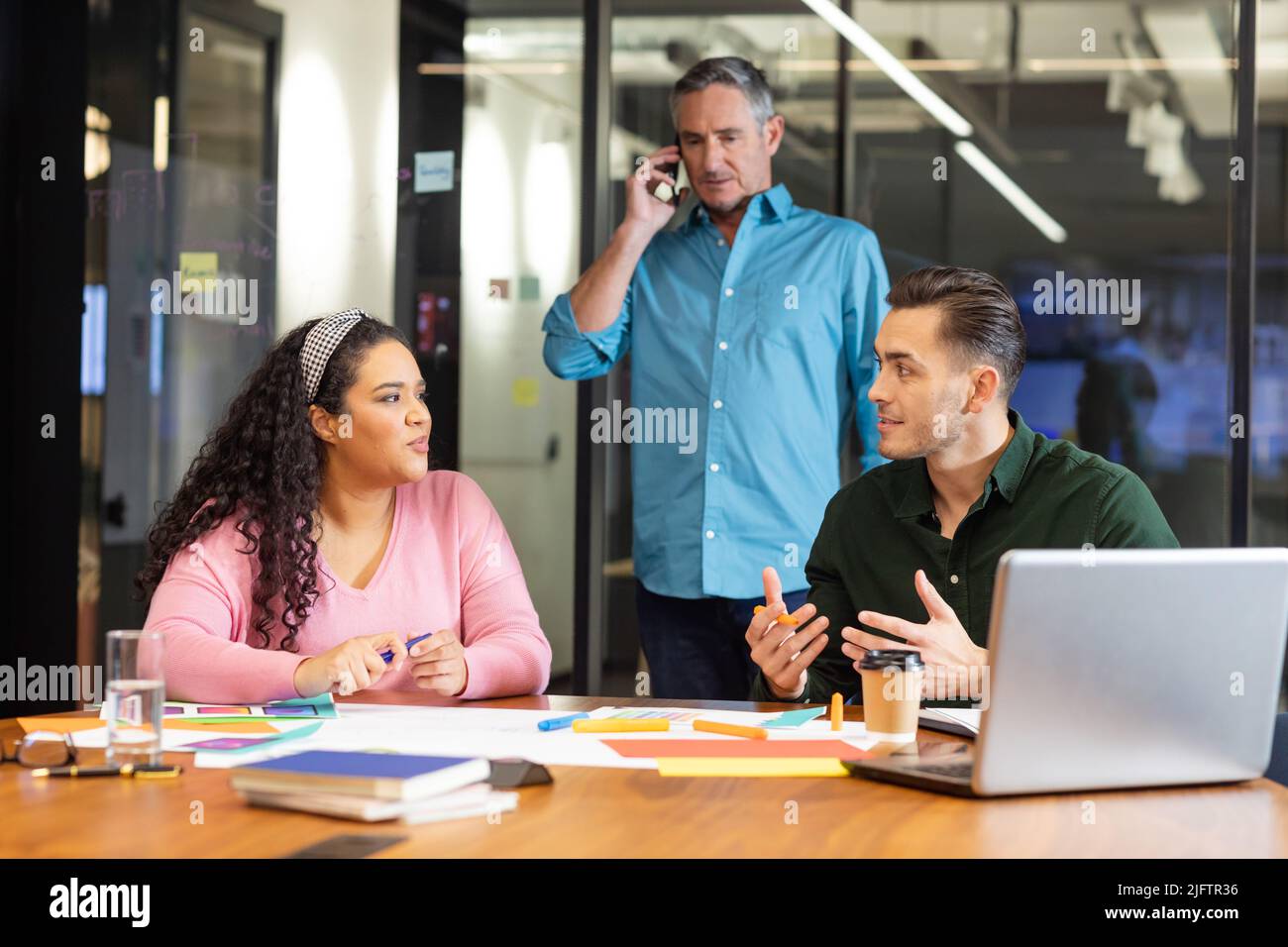Manager parlant sur smartphone en regardant des collègues multiraciaux discuter de la stratégie au bureau Banque D'Images