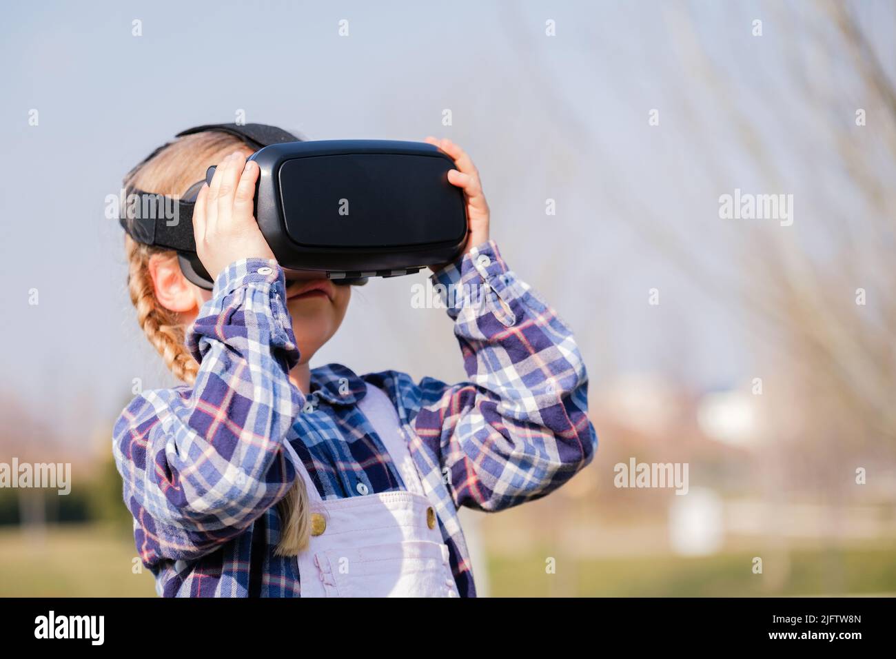 Petite fille avec lunettes de réalité virtuelle. Futur concept de technologie - belle fille avec réalité virtuelle en plein air dans un parc Banque D'Images
