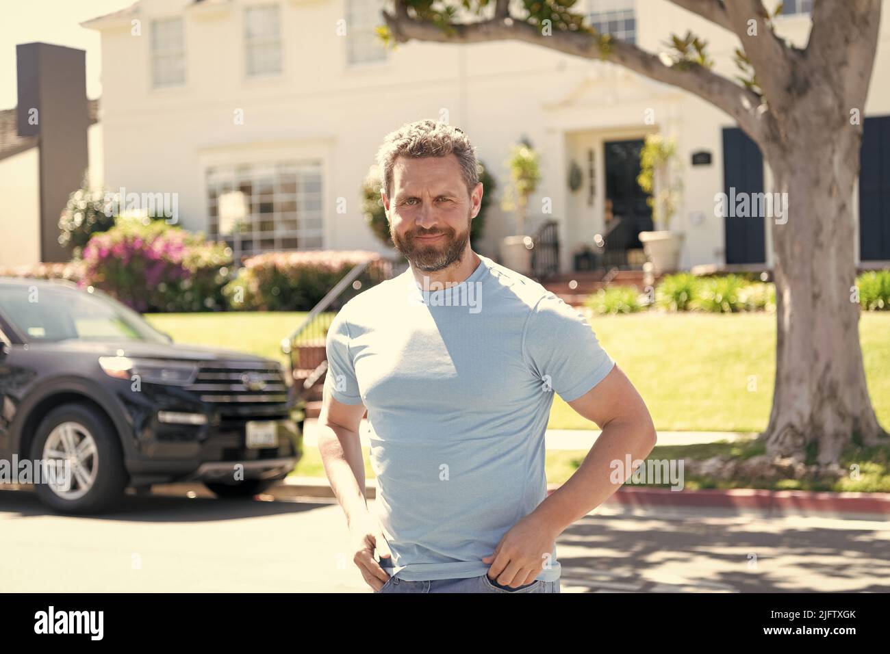 homme barbu souriant dans une chemise bleue décontractée à l'extérieur à la maison et en voiture, bonne humeur Banque D'Images