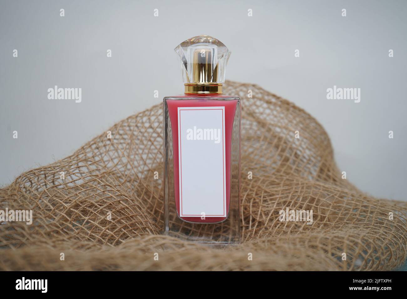 Bouteille de parfum rouge avec rectangle blanc et capuchon doré, sur fond blanc et parfum de toile de jute maquette. Et 3D rendu Banque D'Images