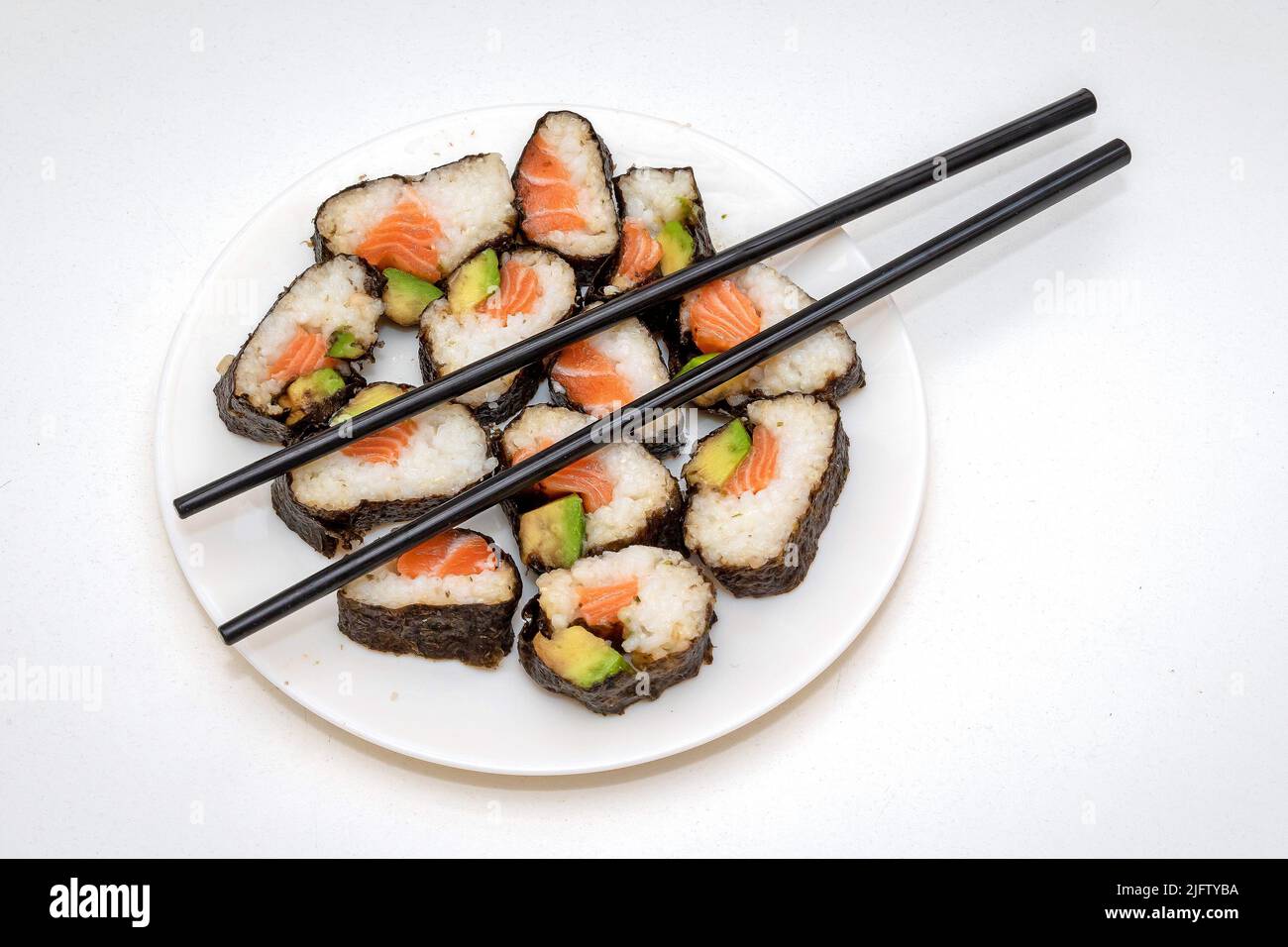 Repas de sushis japonais avec saumon cru et avocat avec baguettes sur une assiette blanche Banque D'Images