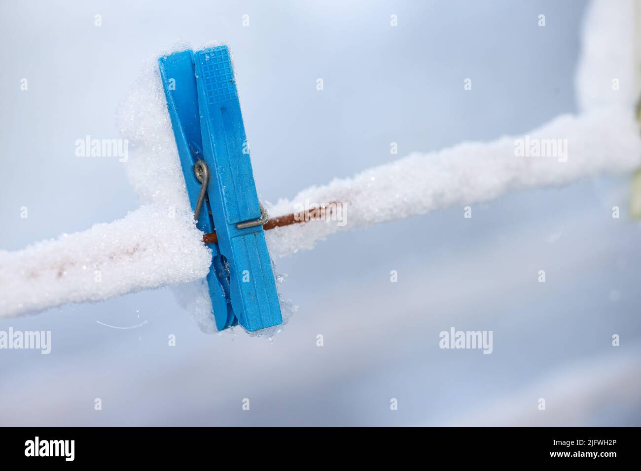 Une cheville en bois bleu surgelé recouverte de neige sur une ligne. Une vieille corde à linge en bois sur une ligne de lavage dans un jardin glacé. Outil de suspension à l'ancienne Banque D'Images
