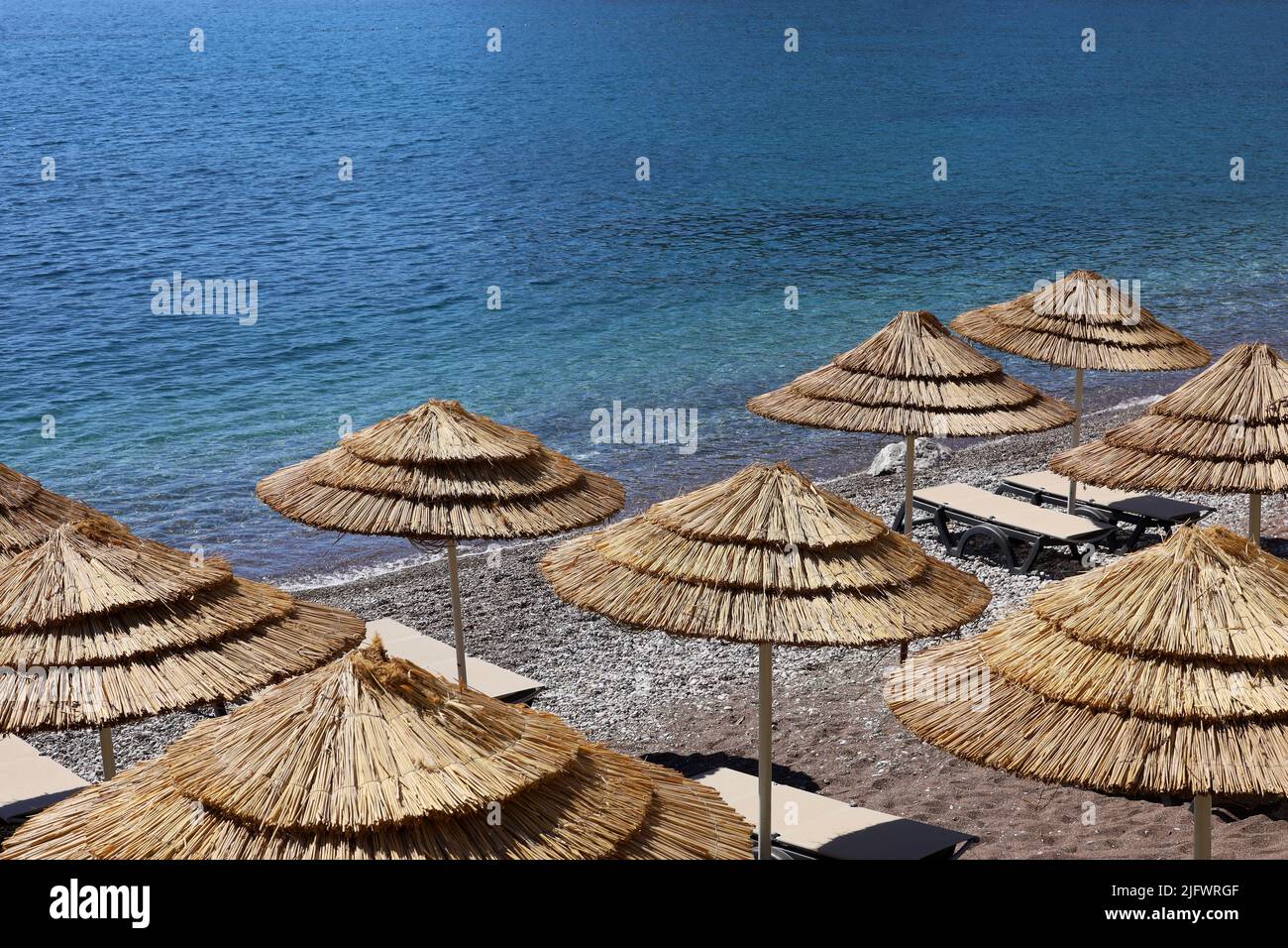 Plage de galets vide avec parasols en osier et chaises longues. Vue pittoresque sur la mer bleue, station balnéaire luxueuse Banque D'Images