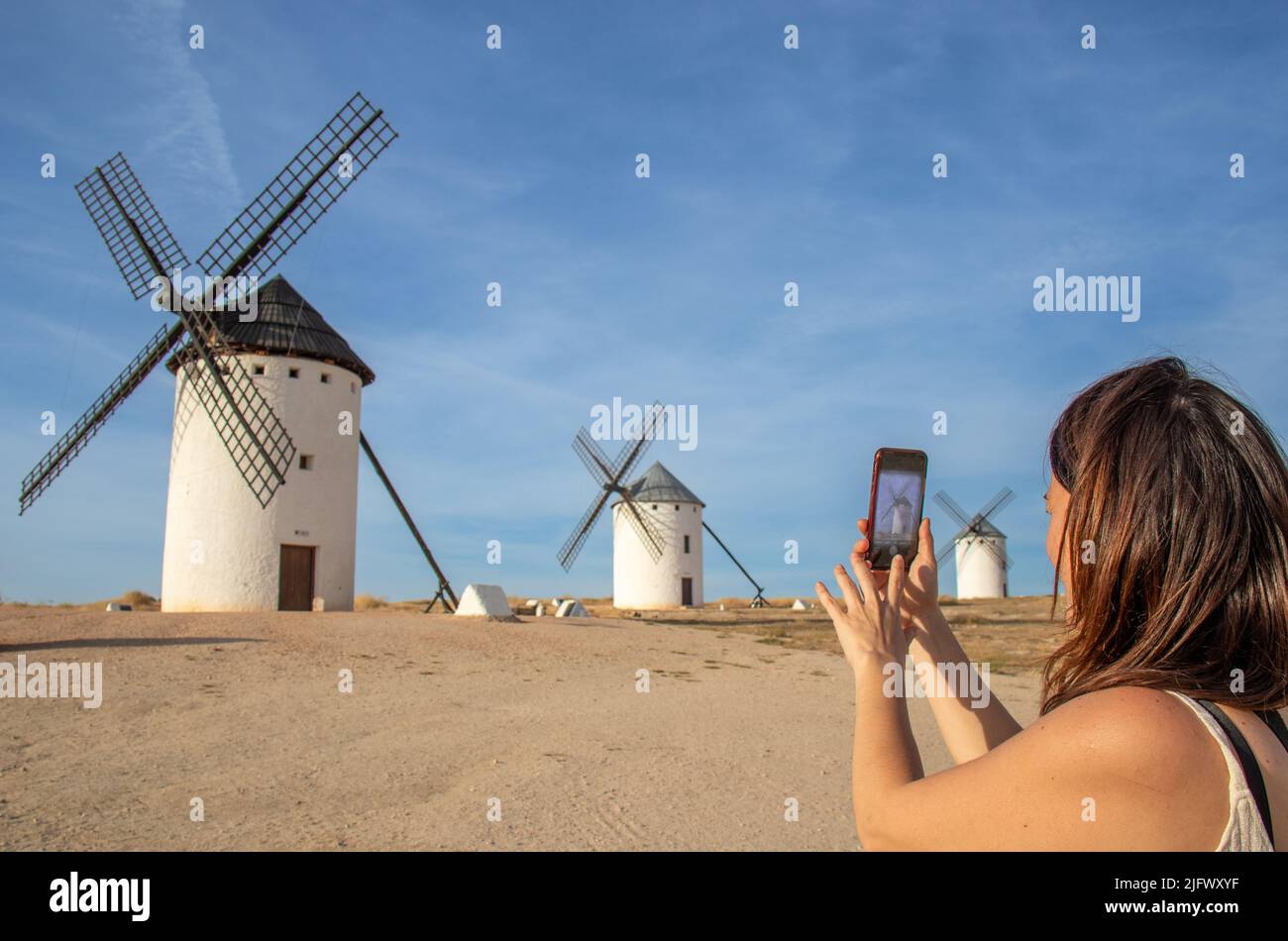Una joven tomando una foto con el móvil de un molino en el cerro molinos de viento de Campo de Criptana, España Banque D'Images