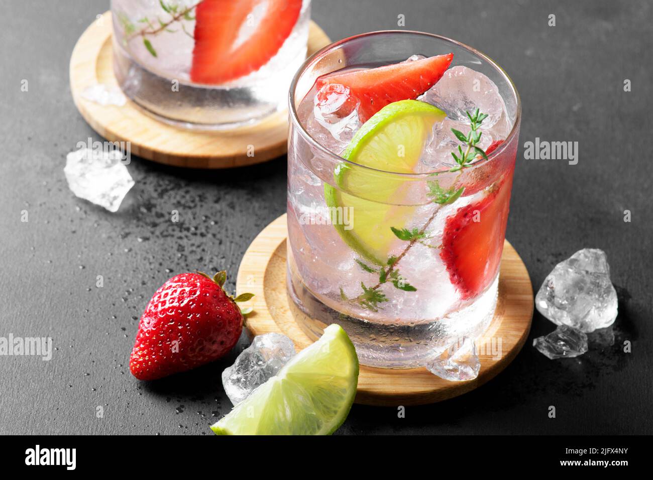 Deux verres avec boisson gazeuse aux fraises d'été ou mojito avec fraise, glaçons et citron vert sur fond sombre Banque D'Images