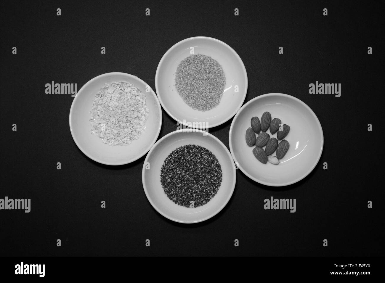Amandes, chia et autres graines végétaliennes saines dans 4 bols ronds en porcelaine blanche sur fond noir Banque D'Images