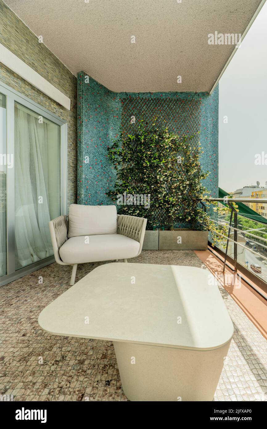 Terrasse avec fauteuils en tissu gris, garde-corps en métal, jardinière, jardin vertical sur un mur bleu, table en marbre et vue sur la ville Banque D'Images