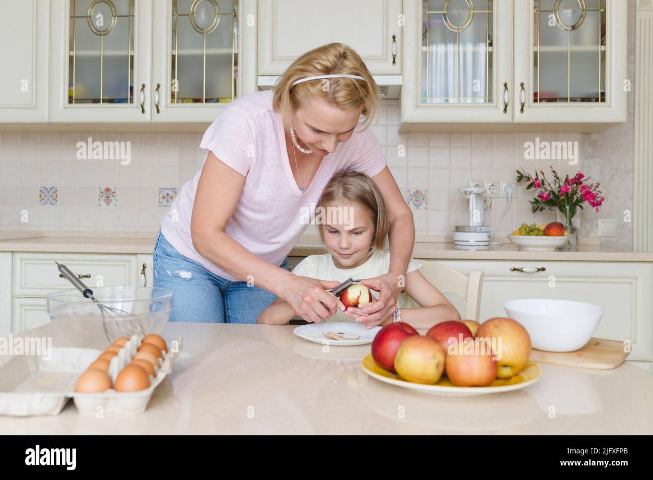 Maman aide sa fille dans la cuisine, lui apprend à peler une pomme. Banque D'Images