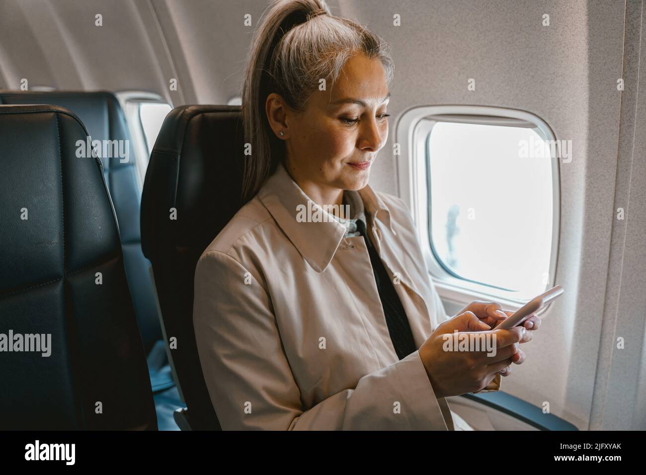 Belle femme asiatique passager assis dans l'avion et utiliser le téléphone pendant l'embarquement Banque D'Images