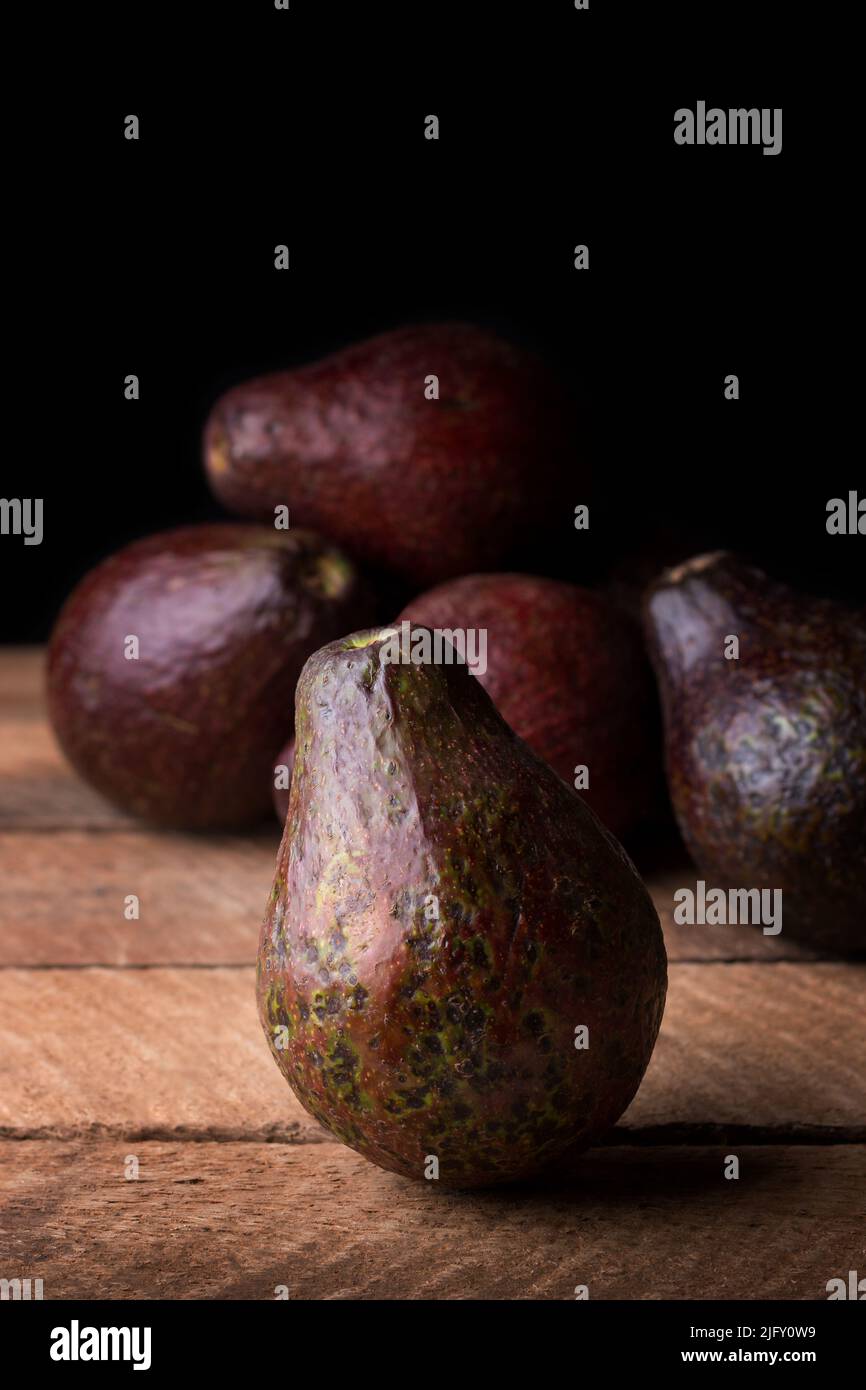 avocats en peau rougeâtre, également connus sous le nom de poire alligator ou de fruit de beurre, fruits frais mûrs sur une table en bois, fond sombre avec espace de copie Banque D'Images