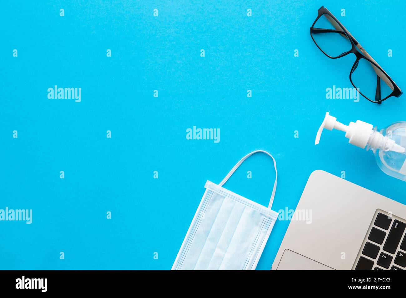 Vue de dessus nouveau masque préventif, gel désinfectant, ordinateur portable et lunettes sur fond bleu avec espace pour le texte ou le design. Coronavirus (COVID- Banque D'Images
