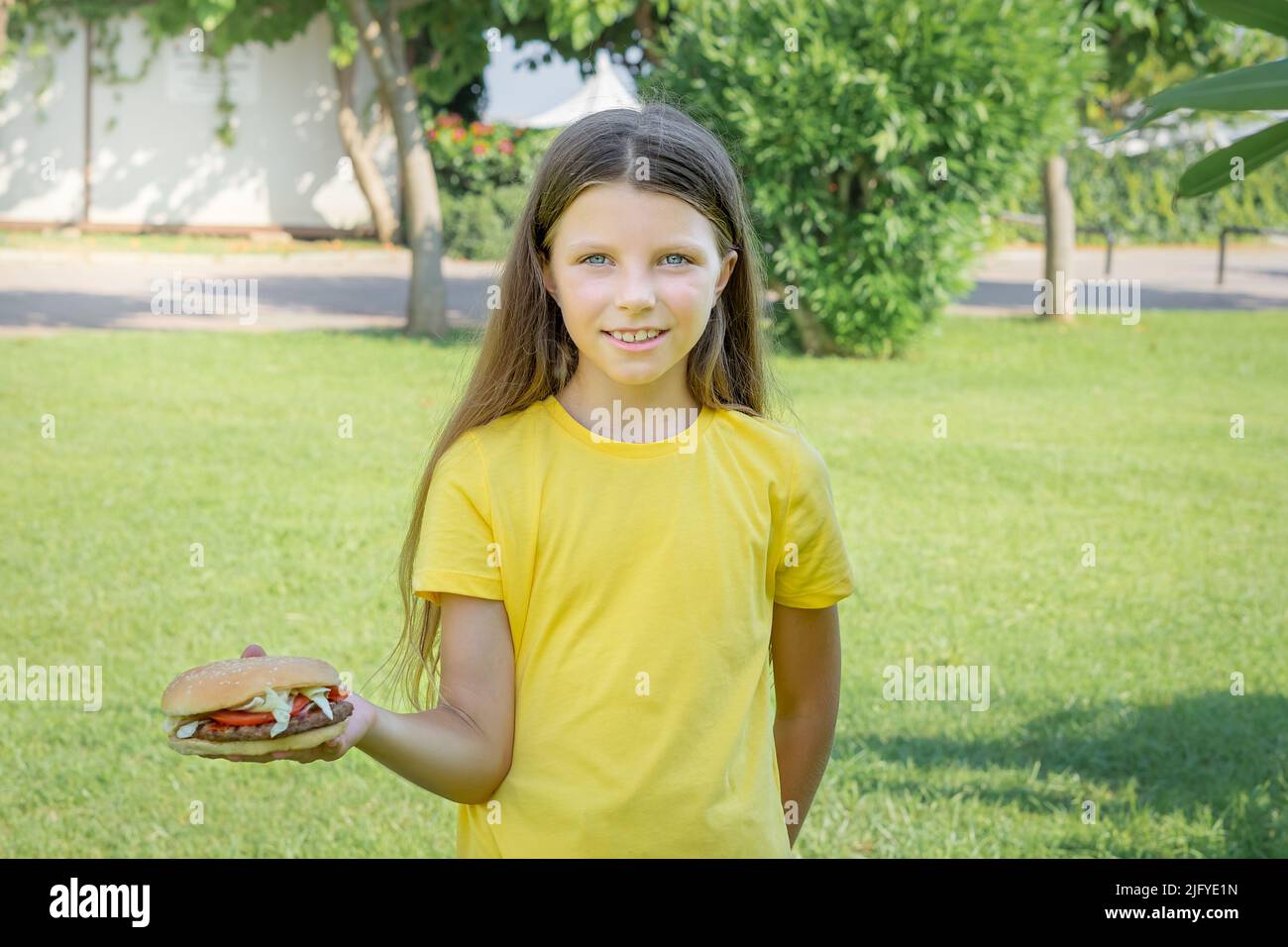 Bonne adolescente mangeant un hamburger dans le parc à l'extérieur. Banque D'Images