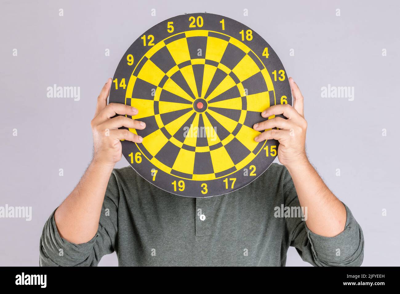 Les gens qui tiennent le dartboard jaune et se cachent son visage. Prise de vue en studio isolée sur fond gris Banque D'Images