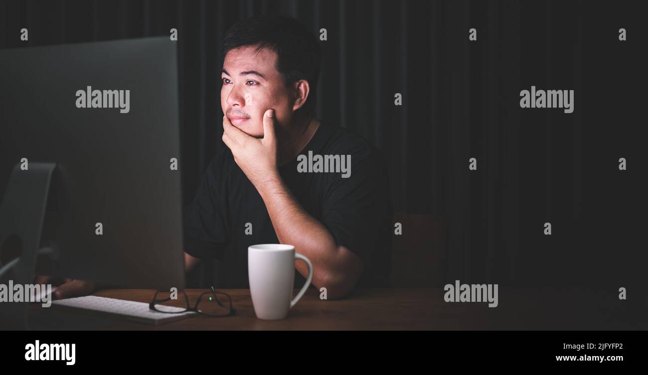 Début de travail dans le concept du matin : homme asiatique travaillant sur ordinateur dans la pièce sombre et regardant à l'écran avec le visage passionnant. Espace sombre pour le texte an Banque D'Images
