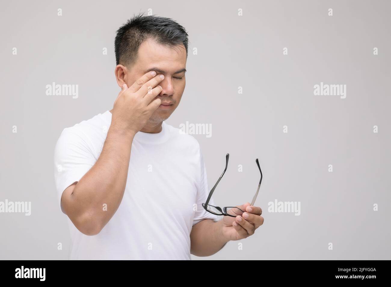Concept d'irritation des yeux : Portrait de l'homme asiatique en posture de fatigue oculaire, irritation ou problème oculaire. Prise de vue en studio isolée sur fond gris Banque D'Images