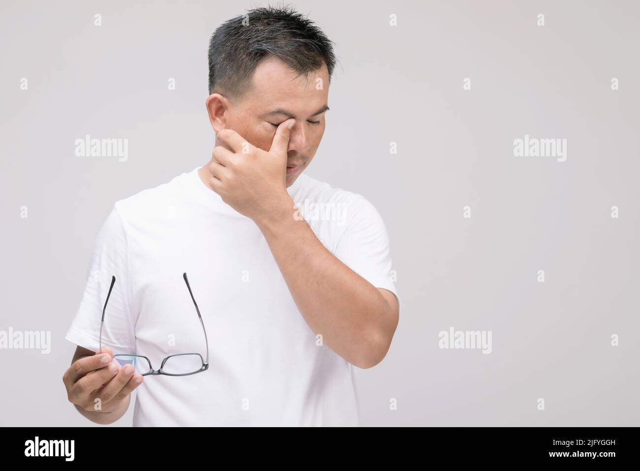 Concept d'irritation des yeux : Portrait de l'homme asiatique en posture de fatigue oculaire, irritation ou problème oculaire. Prise de vue en studio isolée sur fond gris Banque D'Images