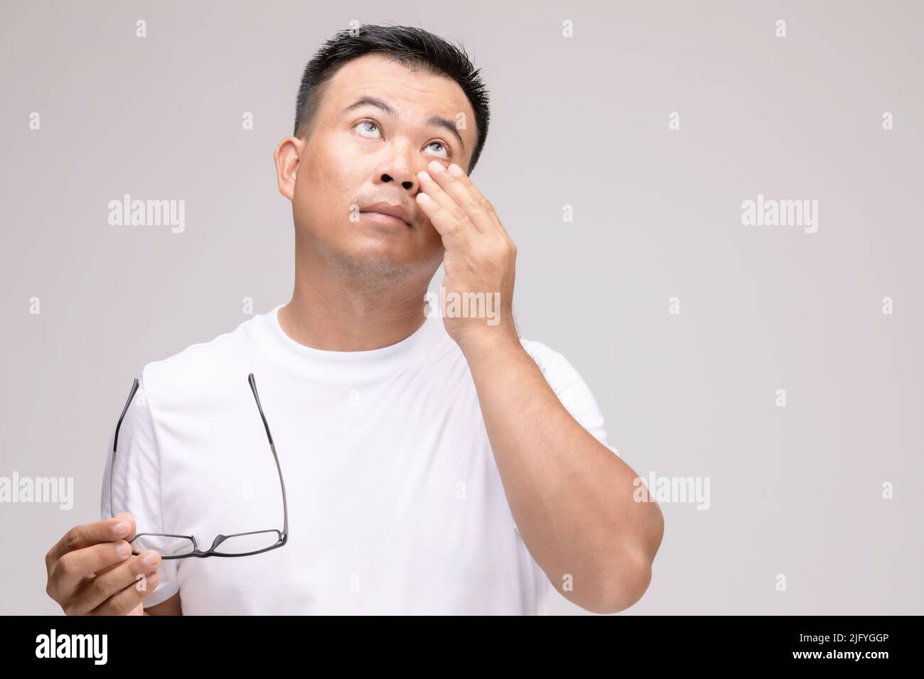 Concept d'irritation des yeux : Portrait de l'homme asiatique en posture de fatigue oculaire, irritation ou problème oculaire. Prise de vue en studio isolée sur fond gris Banque D'Images