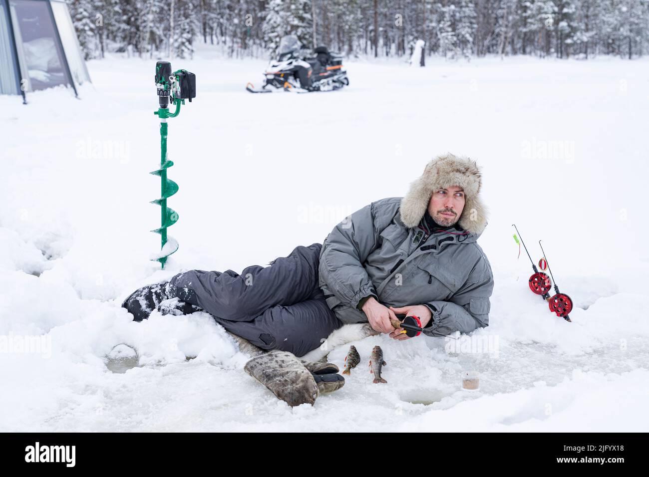 Homme allongé sur la glace tout en pêchant depuis un trou, Laponie, Suède, Scandinavie, Europe Banque D'Images