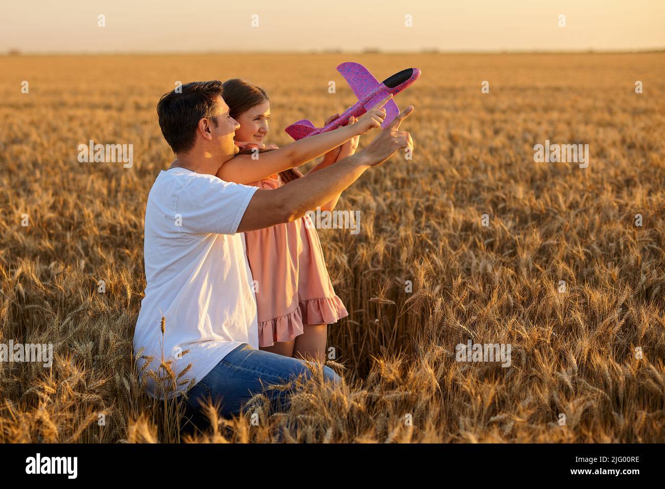 Jolie fille jouant avec l'avion jouet contre le ciel dans le champ de blé Banque D'Images