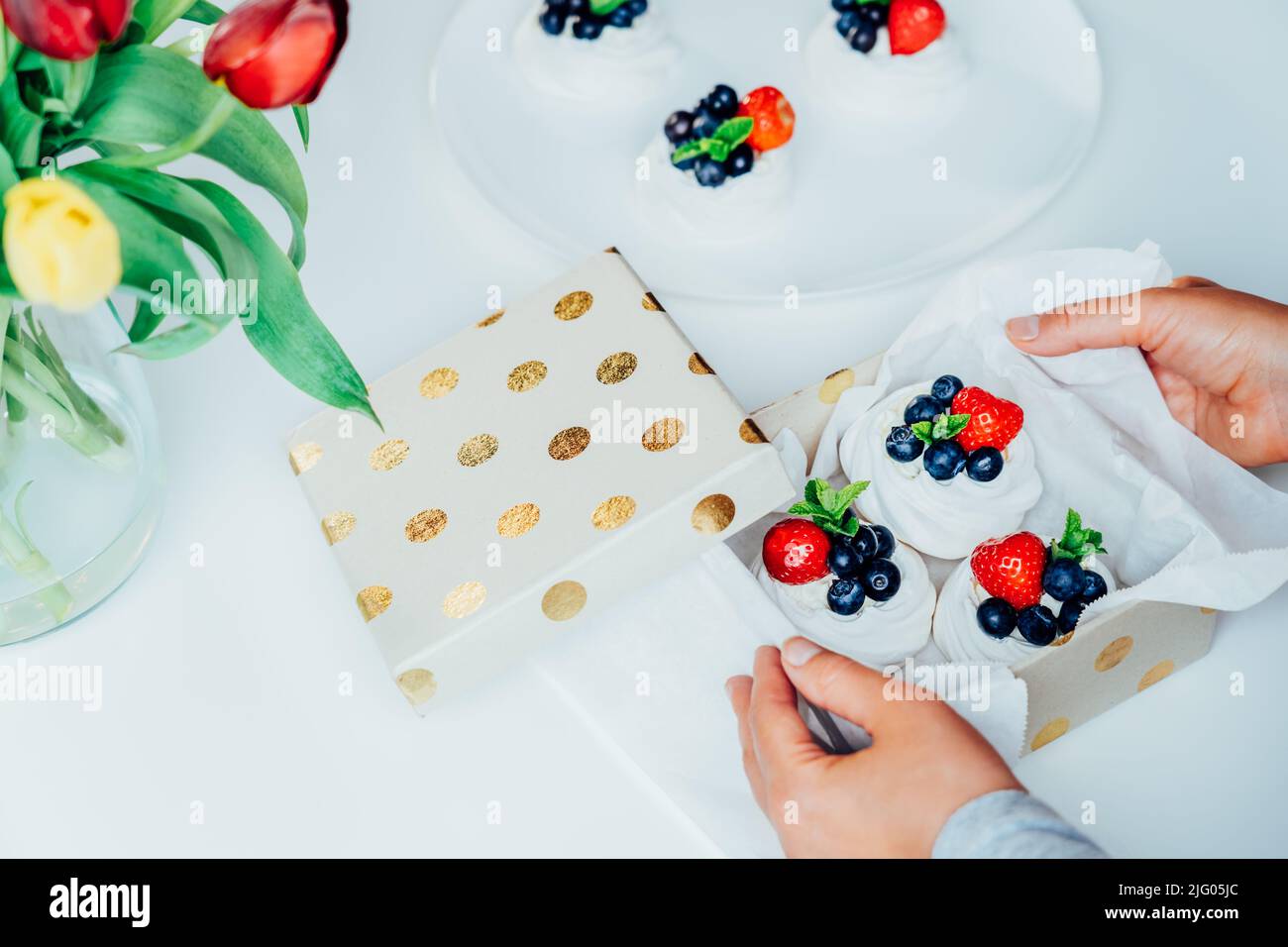 Femme tenant une boîte cadeau avec gâteau de dessert Pavlova meringue aux fraises fraîches et aux myrtilles, décoré de menthe. Cadeau sucré. Repas festifs de Banque D'Images Femme tenant une boîte cadeau avec gâteau de dessert Pavlova meringue aux fraises fraîches et aux myrtilles, décoré de menthe. Cadeau sucré. Repas festifs de Banque D'Images