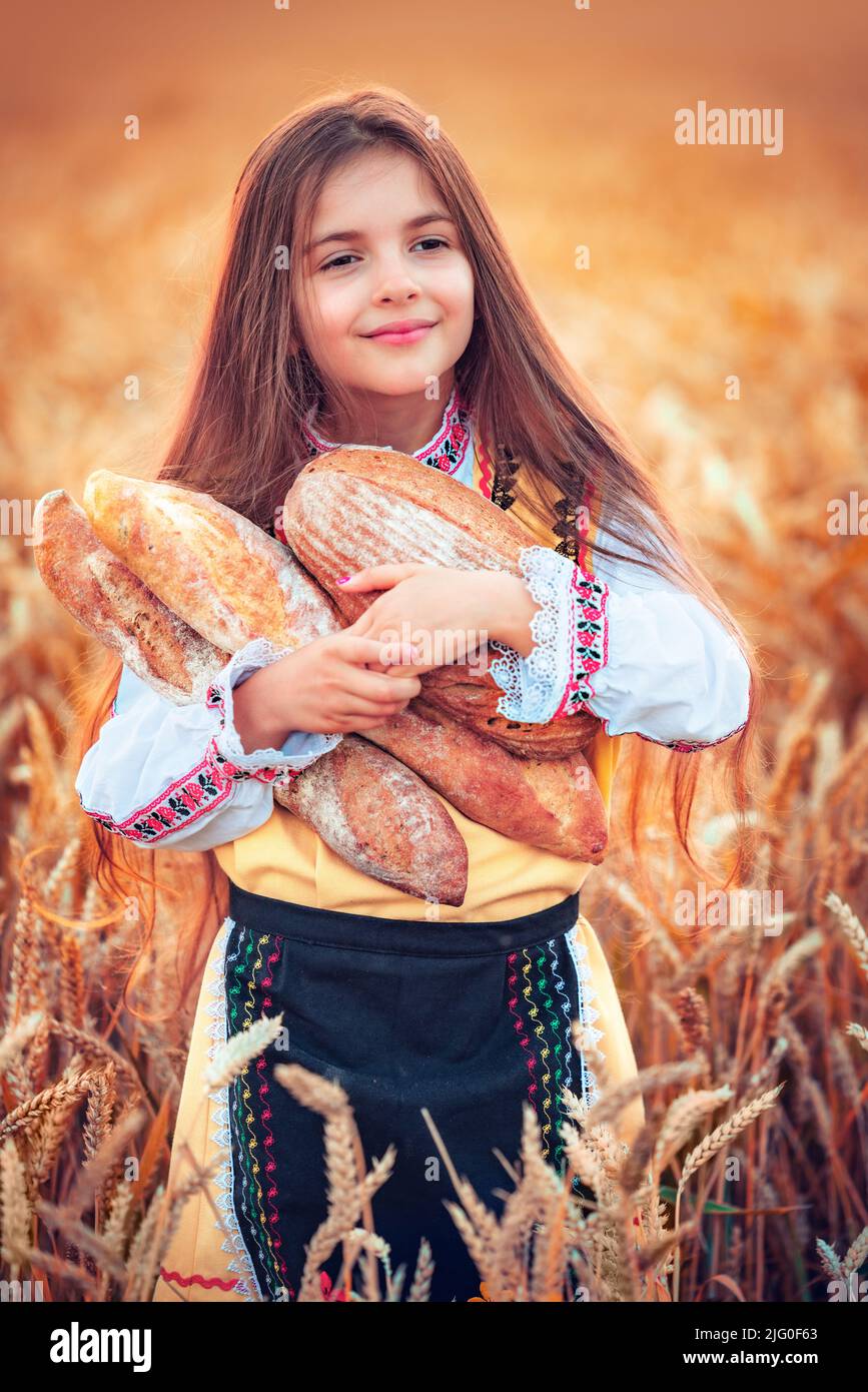 Belle fille femme dans le folklore traditionnel bulgare robe tenant le pain fait maison dans le champ de blé Banque D'Images
