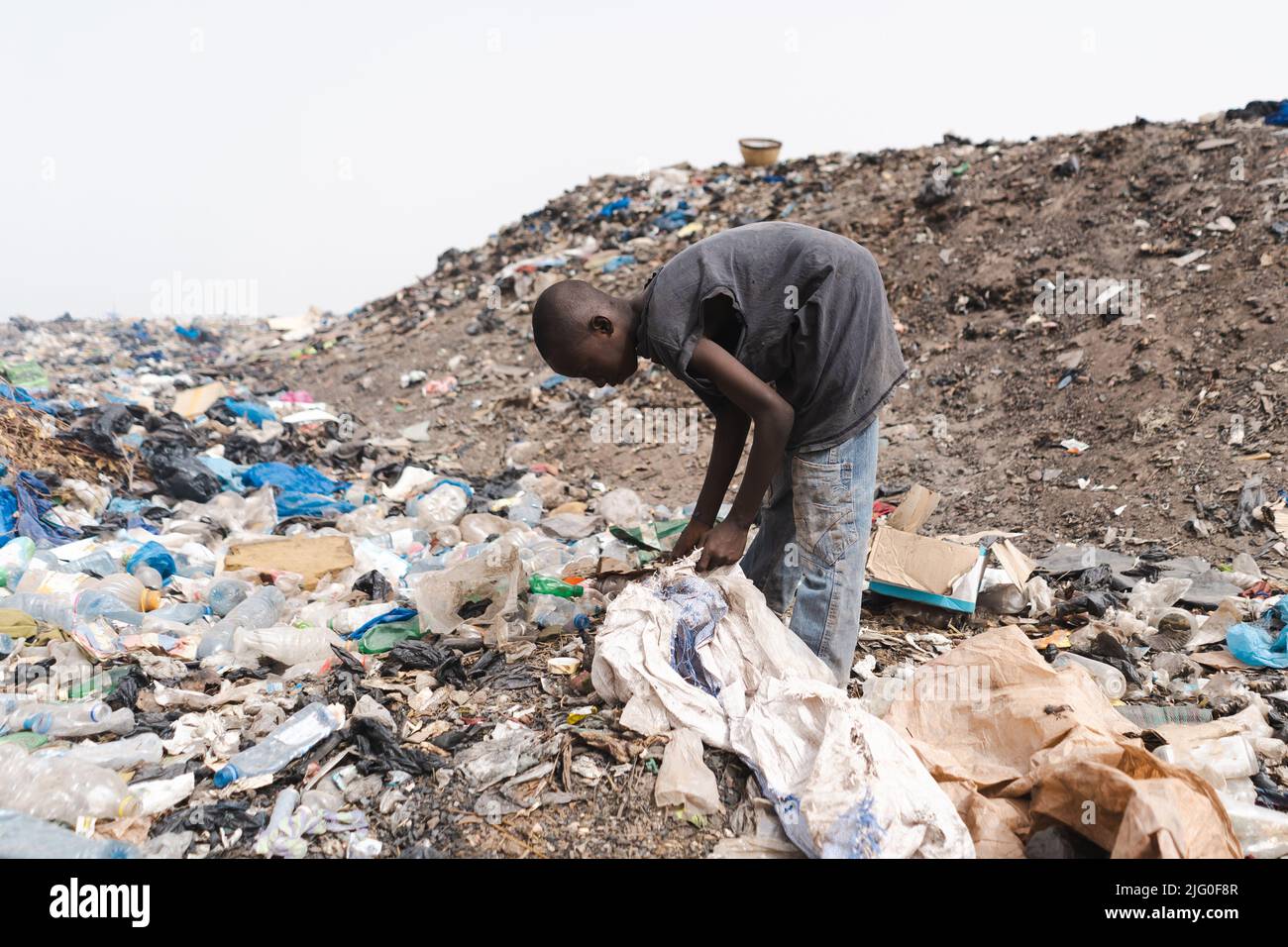 Jeune collecteur africain de déchets remplissant un sac en plastique avec des objets réutilisables dans une décharge urbaine; concept informel de recyclage des déchets Banque D'Images