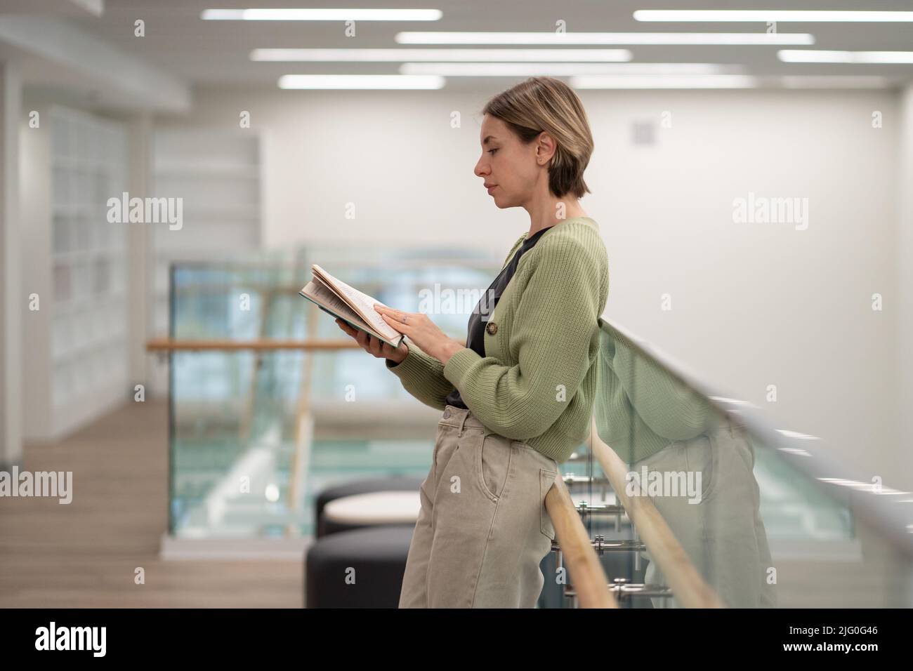 Une femme scandinave pensive d'âge moyen lisant un livre intéressant dans une bibliothèque Banque D'Images