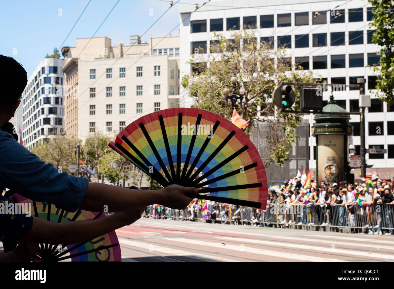 Concentrez-vous sur la fierté du fan de l'arc-en-ciel que quelqu'un dans la foule tient tout en regardant la parade de fierté qui a lieu dans le centre-ville. Banque D'Images