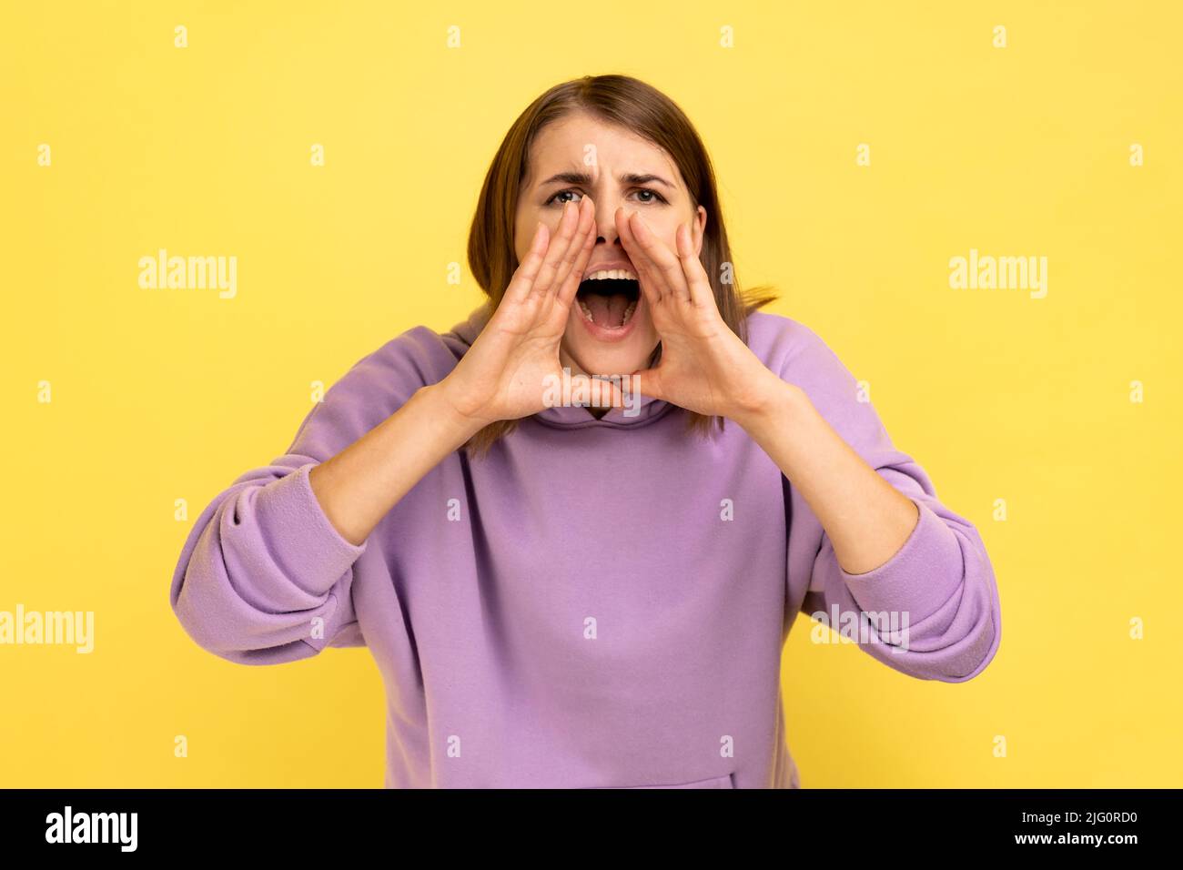 Attention, publicité. Portrait d'une femme hurlant criant sur la vente, annonçant haut et fort message important, portant le pull à capuche violet. Studio d'intérieur isolé sur fond jaune. Banque D'Images