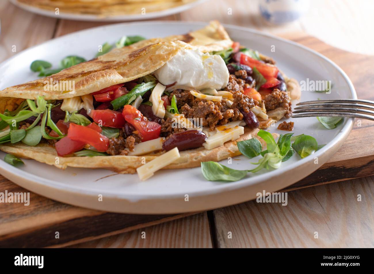 Plat de bœuf haché avec une crêpe ou une crêpe fraîche remplie de haricots rouges, de légumes, de fromage et garnie de crème sure Banque D'Images
