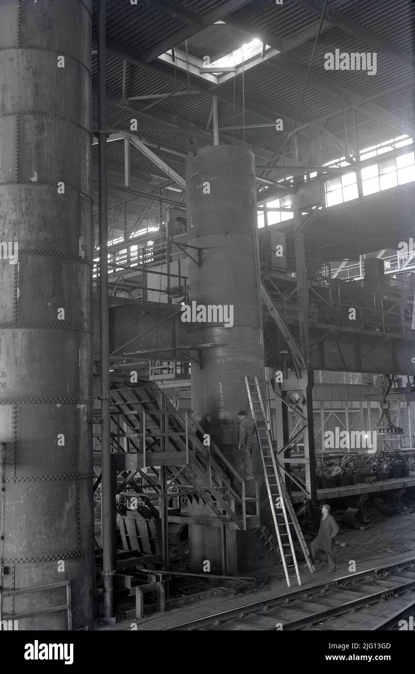 1950s, historique, deux sidérurgistes, l'un sur une échelle, à l'intérieur d'un hangar géant en acier avec la piste rali à Abbey Works, Port Talbot, pays de Galles, Royaume-Uni, le site de la compagnie d'acier du pays de Galles, à cette époque, le plus grand producteur d'acier en Europe. Banque D'Images