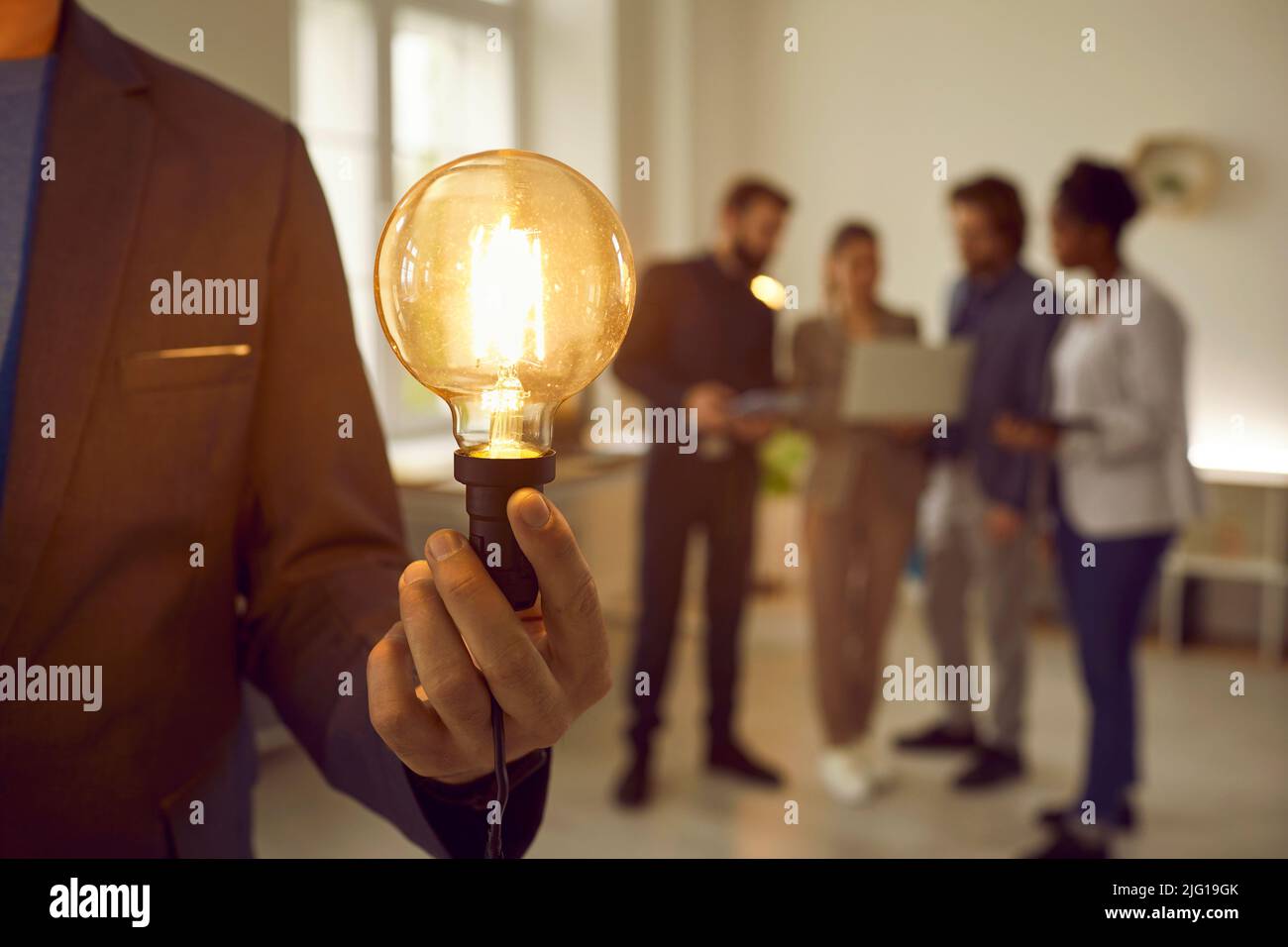 Ampoule lumineuse retenue par un homme d'affaires sur fond d'équipe créative. Banque D'Images