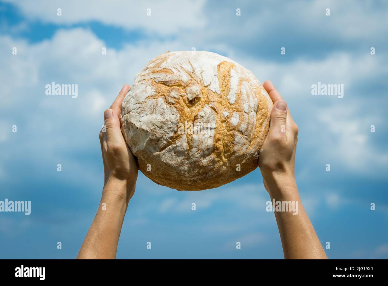 Les mains des femmes tenant le pain cuit maison au-dessus de sa tête sur un ciel bleu d'été. Concept de sécurité alimentaire mondiale. Banque D'Images