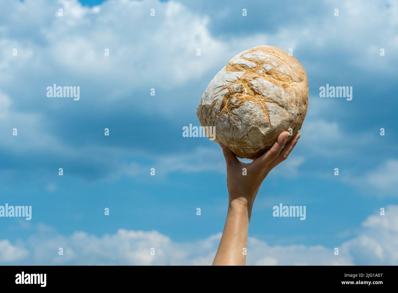 Les mains des femmes tenant le pain cuit maison au-dessus de sa tête sur un ciel bleu d'été. Concept de sécurité alimentaire mondiale. Banque D'Images