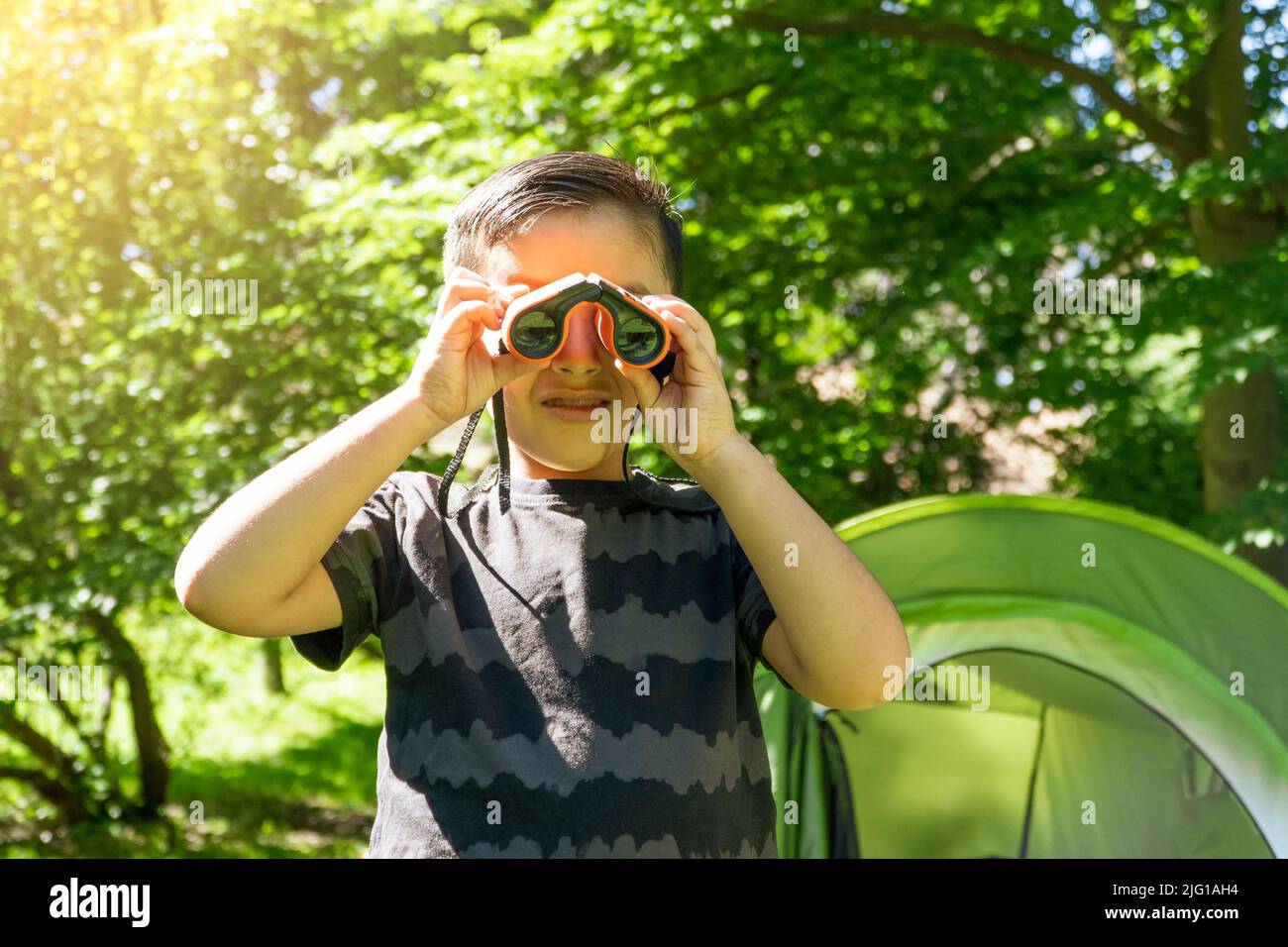 enfant latin vérifiant avec des jumelles lors d'un voyage de camping avec tente en toile sur l'arrière-plan Banque D'Images